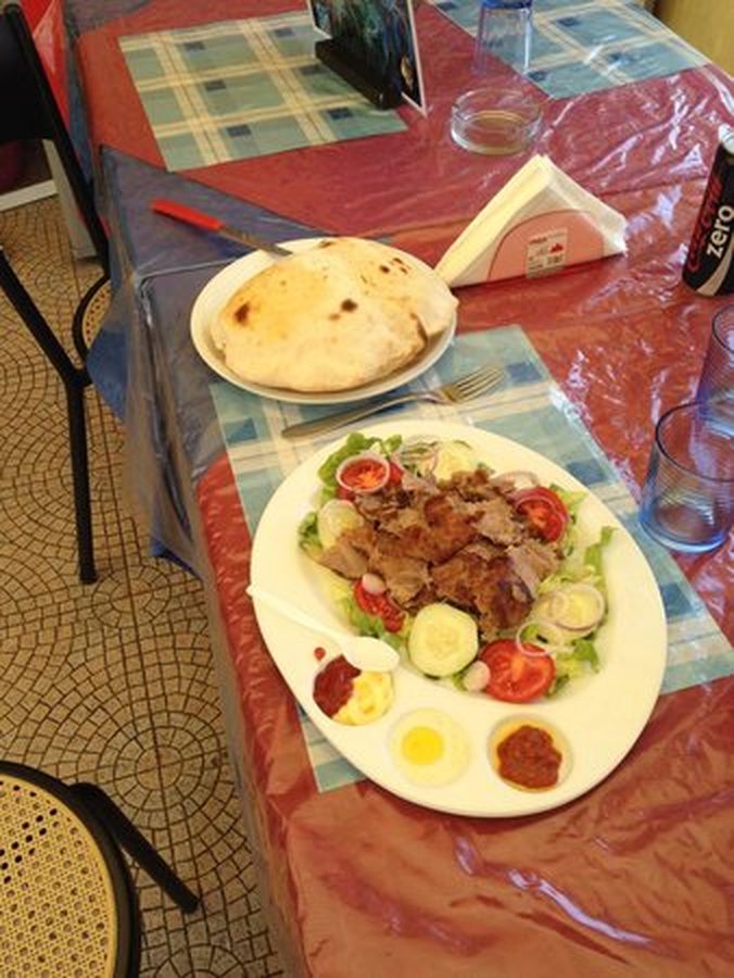 Piatto kebab servito al tavolo: carne affettata su insalata, pomodori e uova, con le salse a parte e il pane caldo accanto.