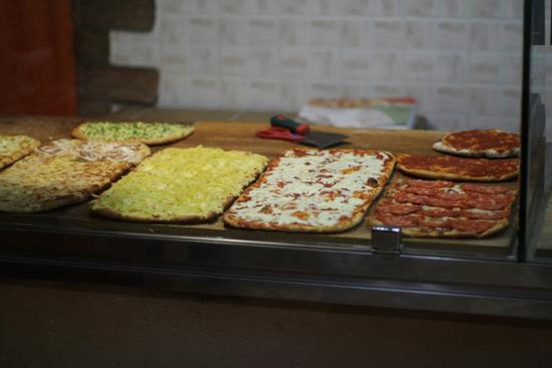 La vetrina della pizza al taglio di Pizzeria Melody: teglie rettangolari di bianca, patate, margherita e pizza rossa allineate sul banco.